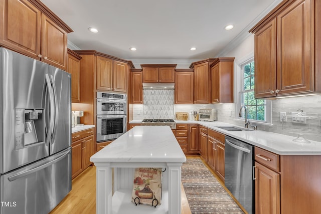 kitchen with crown molding, appliances with stainless steel finishes, a sink, light wood-style floors, and brown cabinetry