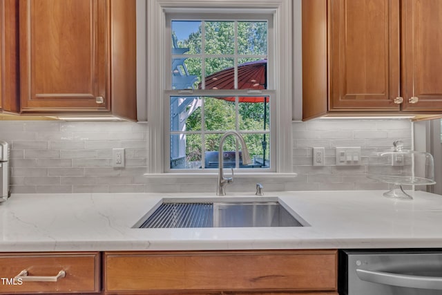 kitchen with a sink, tasteful backsplash, stainless steel dishwasher, and brown cabinetry