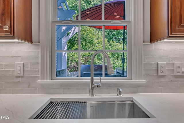 interior details with a sink, light stone counters, decorative backsplash, and brown cabinetry