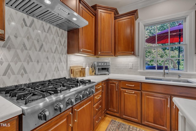 kitchen featuring a sink, stainless steel gas cooktop, brown cabinetry, wall chimney exhaust hood, and backsplash