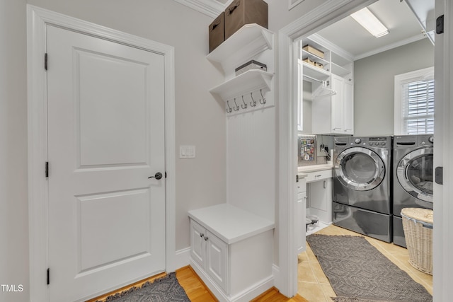 clothes washing area with light tile patterned floors, ornamental molding, cabinet space, and washing machine and clothes dryer