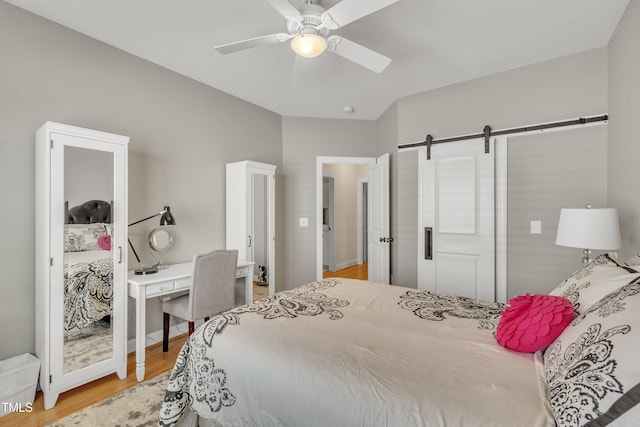 bedroom with a barn door, ceiling fan, and wood finished floors