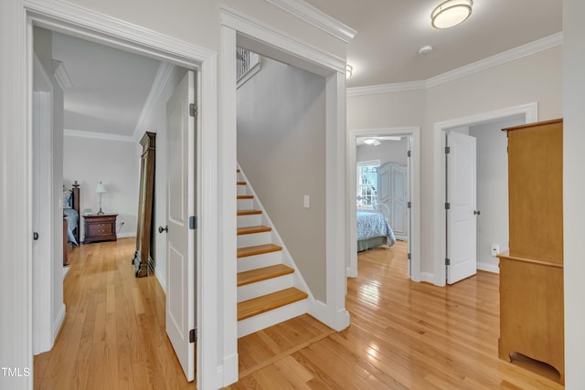 hallway featuring baseboards, ornamental molding, light wood-type flooring, and stairs