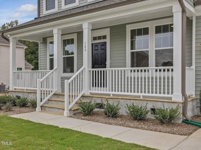 doorway to property featuring a shingled roof, covered porch, and central AC unit