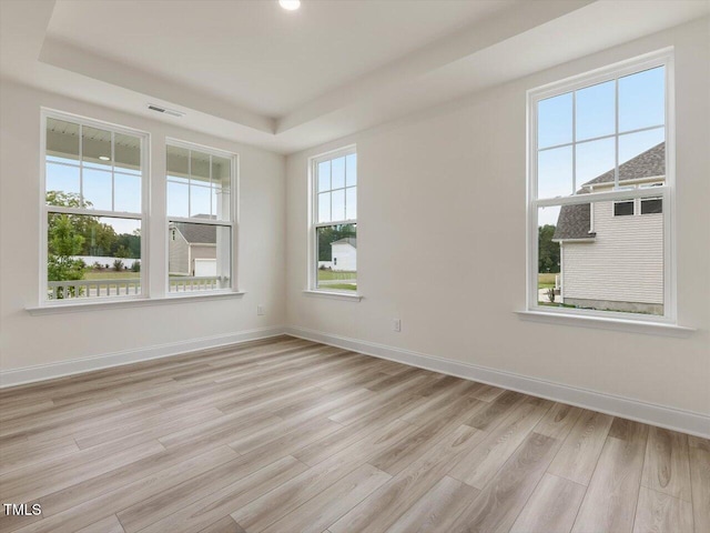 spare room with light wood-type flooring, visible vents, baseboards, and a tray ceiling