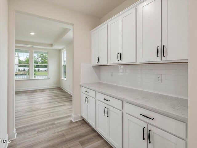 kitchen with tasteful backsplash, light wood-type flooring, white cabinetry, and baseboards