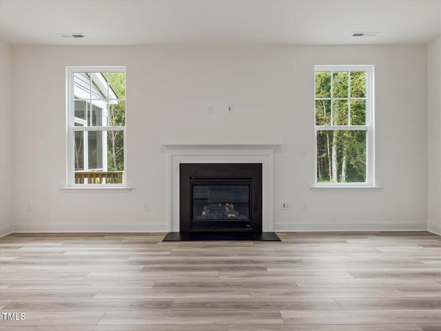 unfurnished living room featuring visible vents, light wood-type flooring, and a wealth of natural light