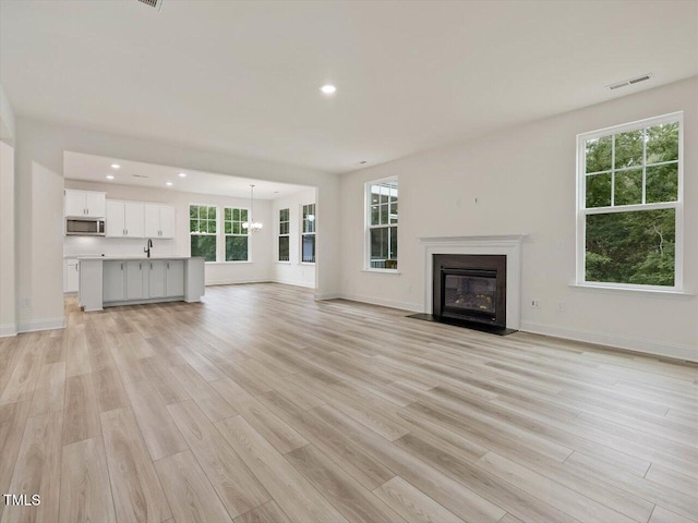 unfurnished living room featuring visible vents, recessed lighting, light wood-style floors, and a fireplace with flush hearth