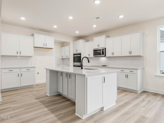 kitchen featuring white cabinets, stainless steel microwave, light wood-style flooring, and a sink