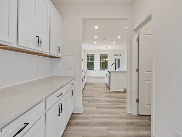 corridor with recessed lighting, an inviting chandelier, a sink, light wood-style floors, and baseboards