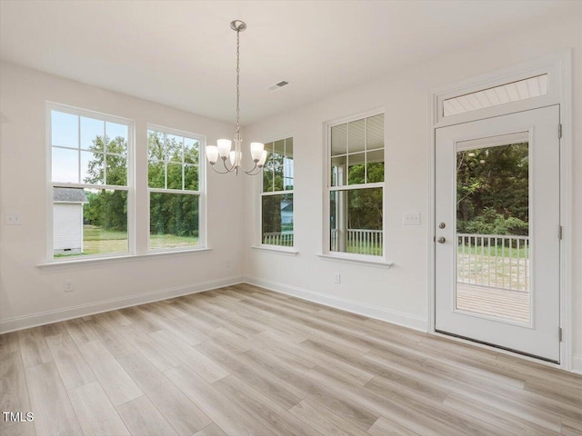 unfurnished dining area featuring a healthy amount of sunlight, visible vents, light wood-type flooring, and an inviting chandelier