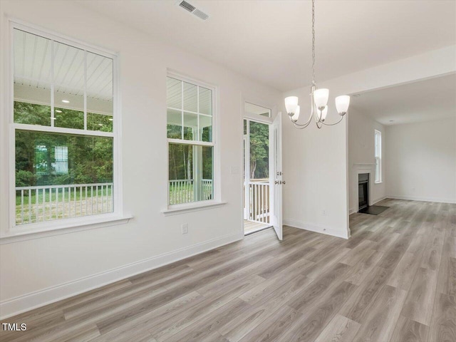 unfurnished dining area featuring an inviting chandelier, light wood-style floors, baseboards, visible vents, and a fireplace with flush hearth