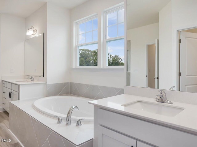 bathroom with two vanities, a bath, and a sink