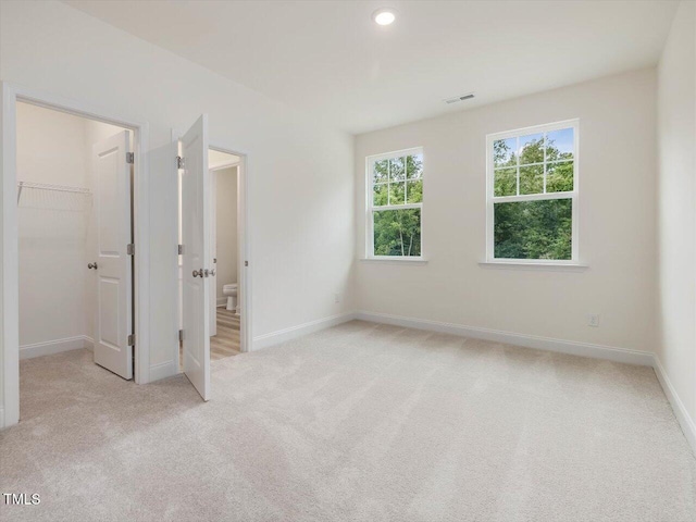 unfurnished bedroom featuring visible vents, a closet, light carpet, baseboards, and a spacious closet