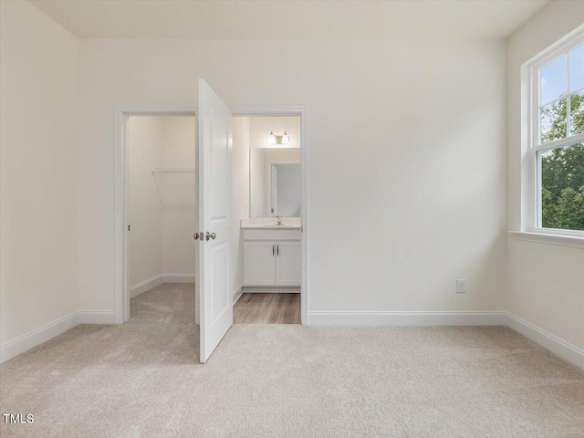 unfurnished bedroom featuring a sink, baseboards, light colored carpet, and a spacious closet