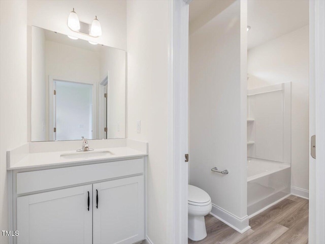 bathroom featuring wood finished floors, bathing tub / shower combination, toilet, vanity, and baseboards
