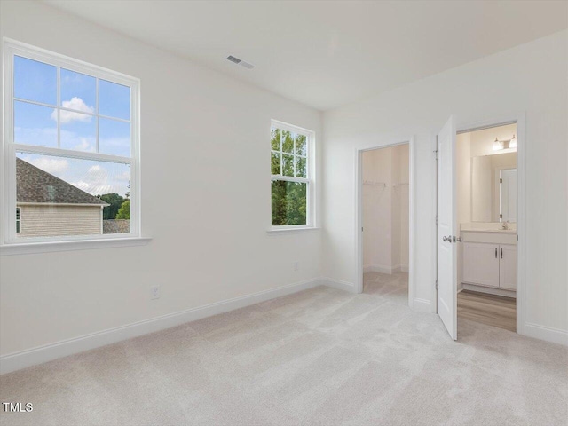 unfurnished bedroom with visible vents, ensuite bathroom, baseboards, light carpet, and a walk in closet
