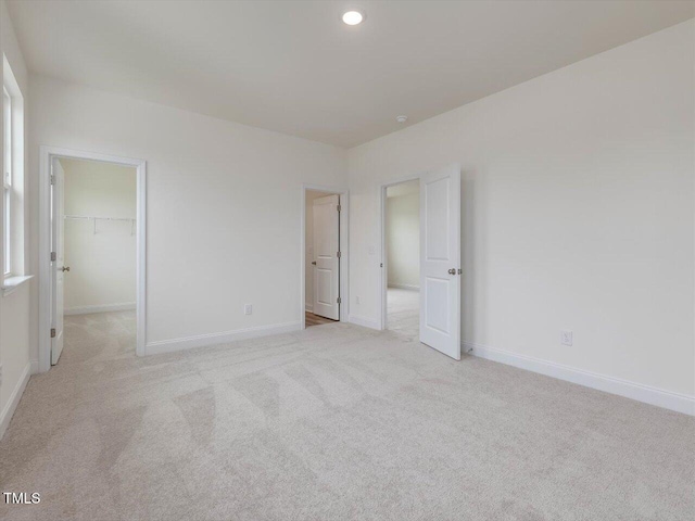 unfurnished bedroom with recessed lighting, a walk in closet, light colored carpet, and baseboards