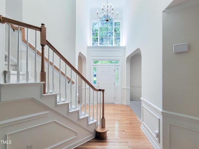 foyer entrance featuring a notable chandelier, arched walkways, light wood-style flooring, a towering ceiling, and stairway