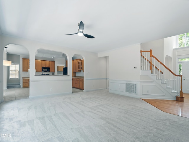unfurnished living room with visible vents, stairway, light colored carpet, arched walkways, and a ceiling fan