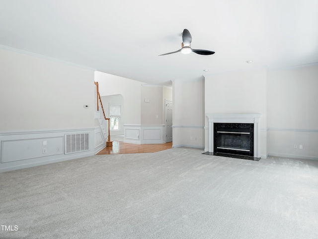 unfurnished living room featuring ceiling fan, light colored carpet, a high end fireplace, visible vents, and stairway