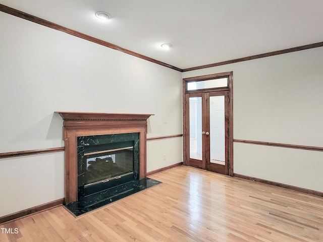 unfurnished living room featuring crown molding, light wood finished floors, a fireplace, french doors, and baseboards