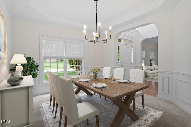 dining area with wainscoting, light carpet, arched walkways, a chandelier, and ornamental molding