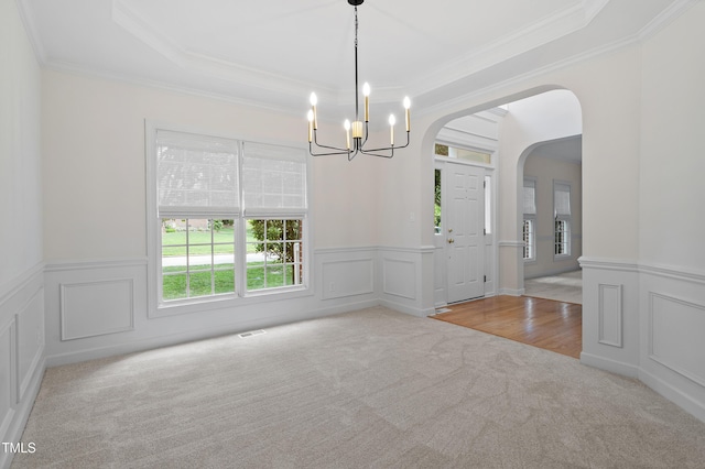unfurnished dining area with an inviting chandelier, ornamental molding, wainscoting, arched walkways, and carpet flooring