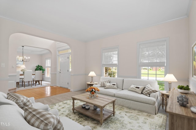 living room featuring arched walkways, a notable chandelier, ornamental molding, and wood finished floors