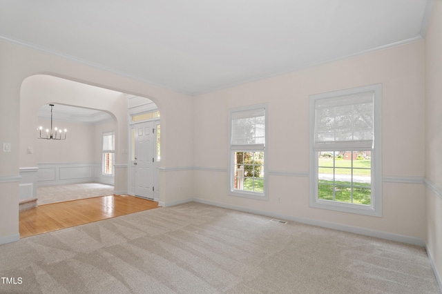 unfurnished living room with wainscoting, wood finished floors, carpet floors, a chandelier, and ornamental molding