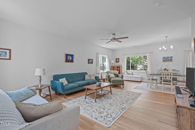 living area featuring light wood-style floors, baseboards, and ceiling fan with notable chandelier