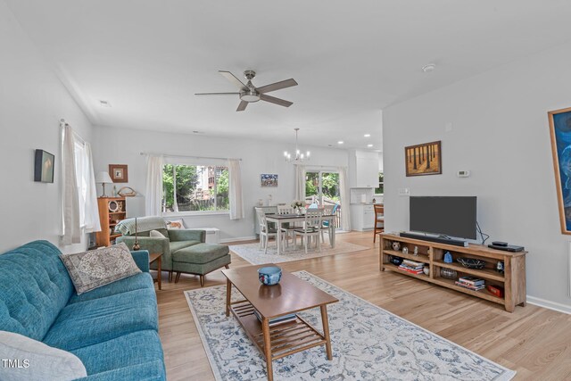 living room featuring recessed lighting, baseboards, ceiling fan with notable chandelier, and light wood-style floors