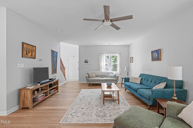 living area featuring a ceiling fan, baseboards, light wood-style flooring, and stairway