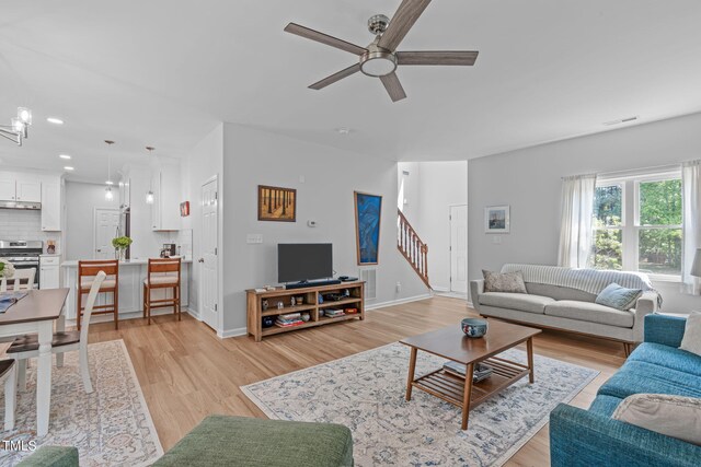 living area featuring visible vents, baseboards, stairway, a ceiling fan, and light wood-style flooring