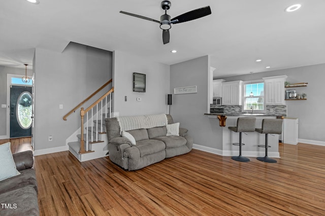 living room featuring stairway, a ceiling fan, light wood finished floors, and recessed lighting