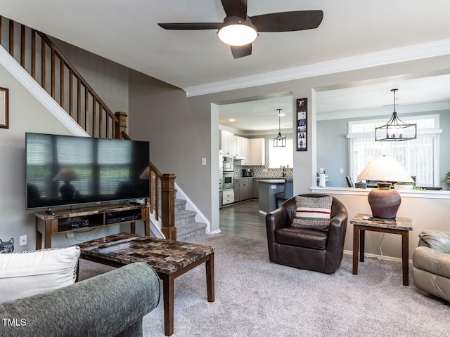 living area featuring carpet floors, ornamental molding, baseboards, stairway, and ceiling fan with notable chandelier