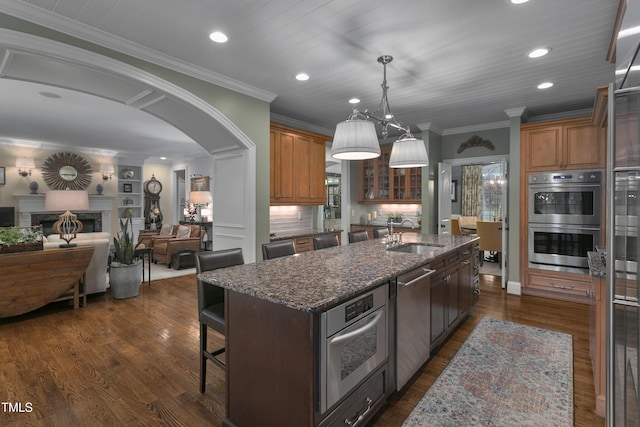 kitchen featuring an island with sink, recessed lighting, arched walkways, a sink, and stainless steel appliances