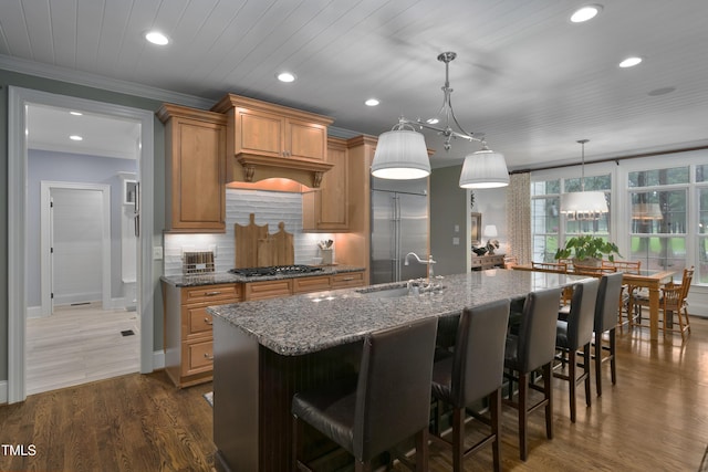 kitchen with a kitchen island with sink, recessed lighting, dark stone counters, a sink, and stainless steel appliances