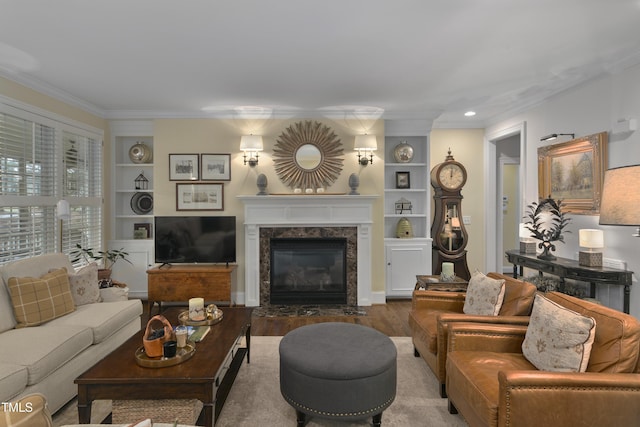 living room with ornamental molding, built in features, wood finished floors, and a premium fireplace