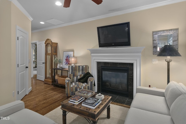 living room featuring ceiling fan, crown molding, a tiled fireplace, wood finished floors, and recessed lighting