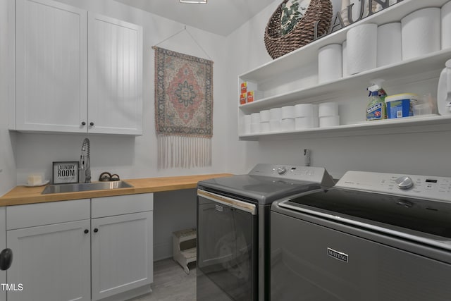 laundry area with a sink, cabinet space, light wood finished floors, and washing machine and dryer