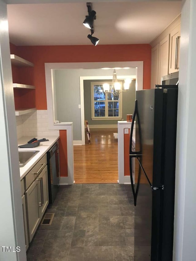 kitchen with tasteful backsplash, a sink, light countertops, black appliances, and an inviting chandelier