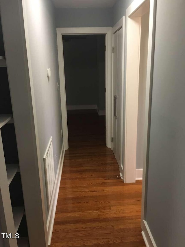hall featuring visible vents, wood finished floors, and baseboards
