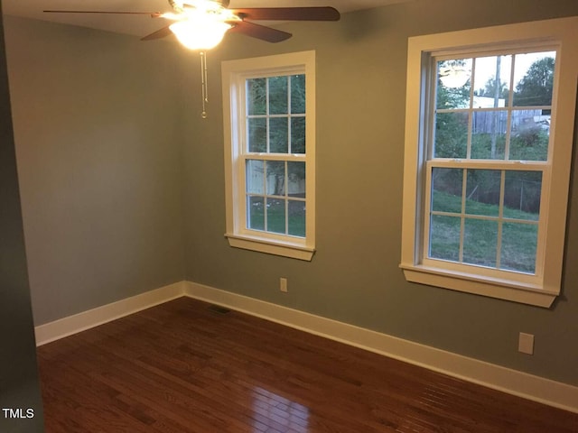 empty room featuring baseboards, ceiling fan, a healthy amount of sunlight, and dark wood-type flooring