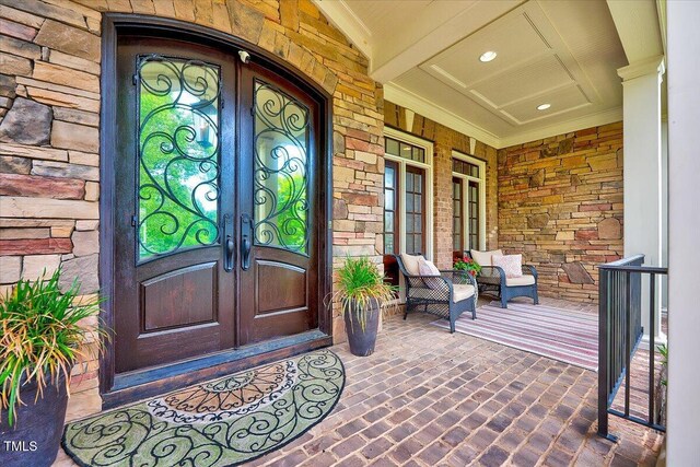 doorway to property featuring a porch, brick siding, and french doors