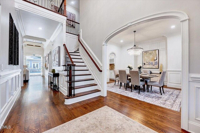 foyer featuring dark wood-style flooring, crown molding, arched walkways, an inviting chandelier, and a decorative wall