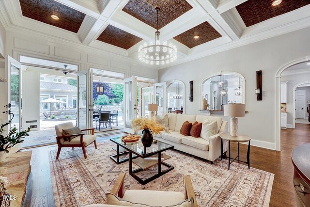 living area featuring arched walkways, an inviting chandelier, ornamental molding, and coffered ceiling