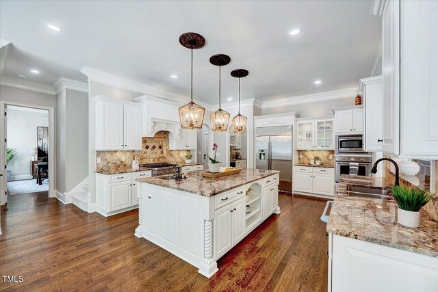 kitchen with built in appliances, white cabinetry, a sink, and backsplash