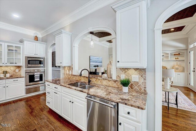 kitchen with crown molding, arched walkways, a sink, a warming drawer, and stainless steel appliances