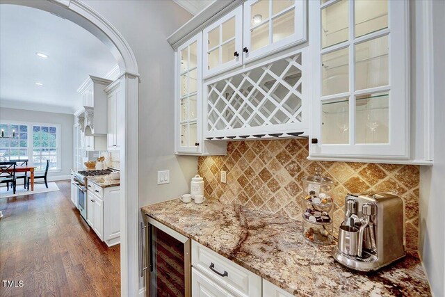 bar featuring arched walkways, dark wood finished floors, high end stainless steel range, a bar, and beverage cooler